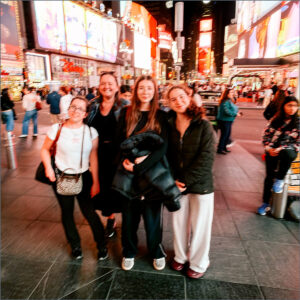 Group of Sixth Form students posing together at night in Times Square with bright billboards behind them, all smiling at the camera.