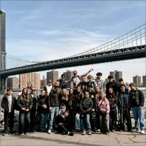 Group of Sixth Formers posing on a riverside with the Brooklyn Bridge and skyline in the background