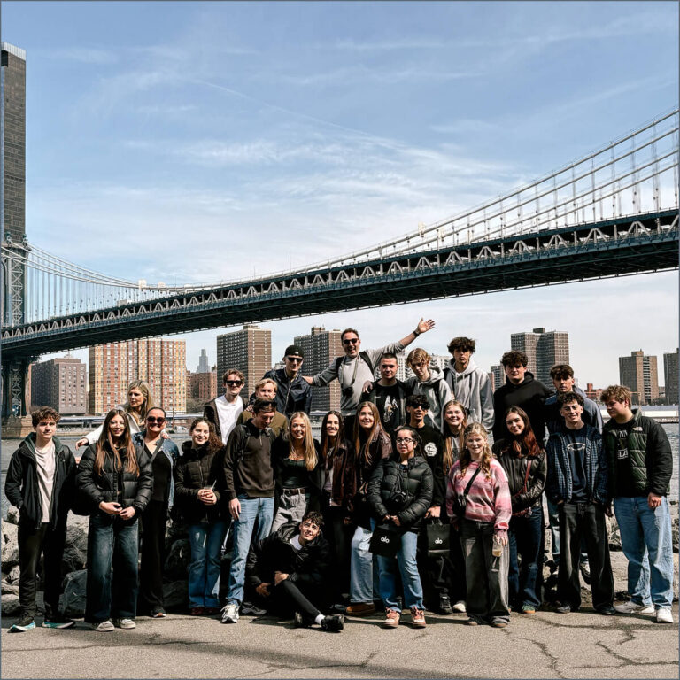 Group of Sixth Formers posing on a riverside with the Brooklyn Bridge and skyline in the background