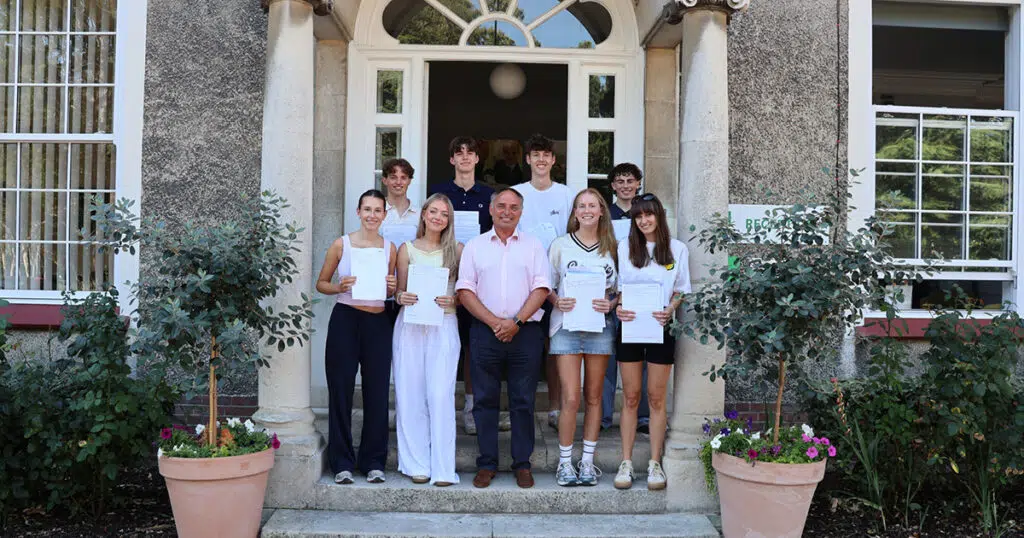 Group of students and a man stand on front steps holding certificates outside a stone building.